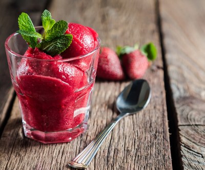 Ein Glas Erdbeersorbet mit Minze und ein Löffel auf einem Tisch