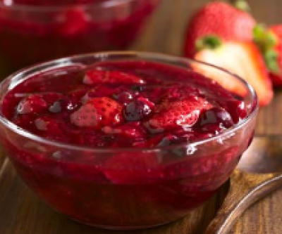 Beerengrütze in einer Glasschüssel auf einem Holztisch. Daneben ein Holzlöffel und geschnittene Erdbeeren